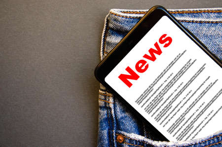 News. Reading the news. The inscription red news on the smartphone screen lies in a jeans pocket. A smartphone with a red inscription news sticks out of a jeans pocket on a black backgroundの写真素材