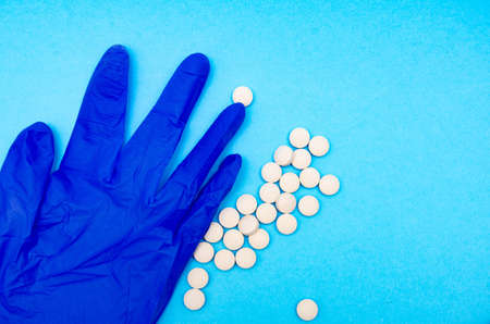 A medical blue glove and white round pills lie on a blue background in macro view from above and at an angle. Crumpled gloveの写真素材