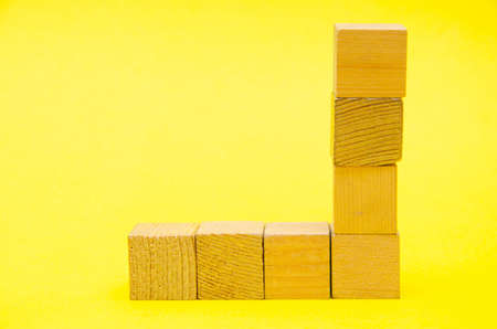 Wooden cubes on a yellow background. Four identical cubes lie on the table horizontally and vertically forming a right angle. Cubes are in the form of a right angle.の写真素材