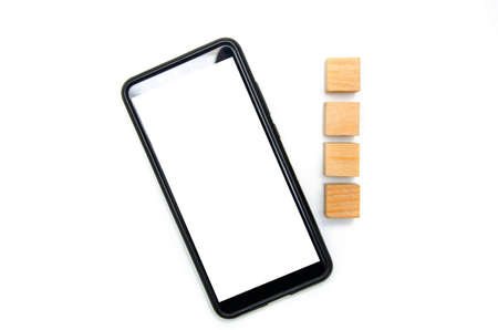 Wooden cubes and smartphone on a white background. The smartphone lies to its right four cubes directly and at an angle the smartphone in the macro white screen of the smartphoneの写真素材