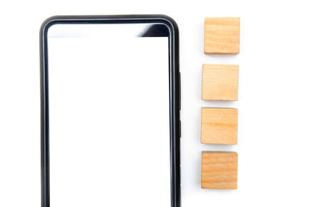 Wooden cubes and smartphone on a white background. The smartphone lies to its right four cubes directly and at an angle the smartphone in the macro white screen of the smartphoneの写真素材