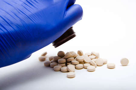 A male hand in blue medical gloves pours out, pours out of a can, a container, white round pills on...