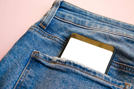 White screen smartphone in jeans pocket. Smartphone place for text. Smartphone in a pocket on a pink background. Copy spaceの写真素材