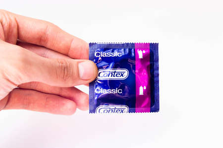 June 2020. Kiev, Ukraine. Contex classic condoms on a white background. Male hand holds one condom and condom package in close-up on a white backgroundのeditorial素材
