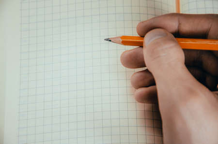 Men's hands, forearm hold a pen, notebook, smartphone. Hands write in notebook in a cell ideas, plans, tasks. Kick on a notebook, break, bend. CopySpace Copy Space Orange, diary. Work with tasks.の写真素材