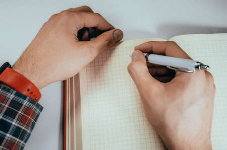 Men's hands, forearm hold a pen, notebook, smartphone. Hands write in notebook in a cell ideas, plans, tasks. Kick on a notebook, break, bend. CopySpace Copy Space Orange, diary. Work with tasks.の写真素材