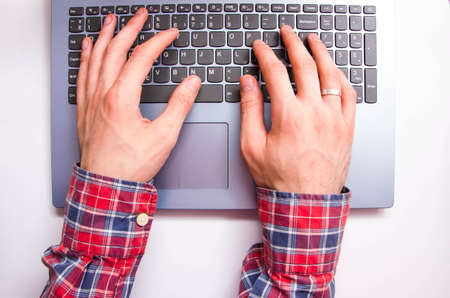 Men's hands in a shirt in a cage lie on the keyboard on a laptop from a first-person view from...