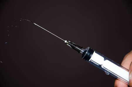 Syringe with a needle on a gray dark background. A drop, a stream flows from a syringe needle. Macro