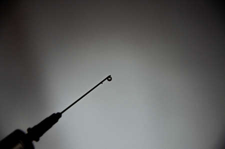 Syringe with a needle on a gray dark background. A drop, a stream flows from a syringe needle. Macro