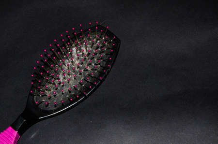 Comb with a red pen on a black background. There are many lengths of blond hair on the rosace. Hair problems. Hair loss. Comb in the hand and on the tableの写真素材