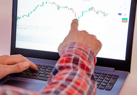 Trading on the exchange. Men's hands in a plaid shirt behind a laptop show on the graph. On-screen...