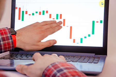 Trading on the exchange. Men's hands in a plaid shirt behind a laptop show on the graph. On-screen...