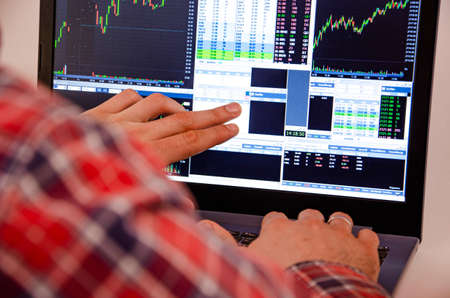 Trading on the exchange. Men's hands in a plaid shirt behind a laptop show on the graph. On-screen...