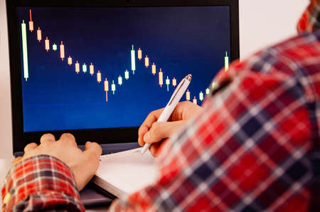 Trading on the exchange. Men's hands in a plaid shirt at a laptop. On-screen rates, promotions....