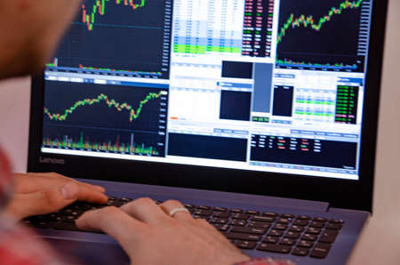 Trading on the exchange. Men's hands in a plaid shirt at a laptop. On-screen rates, promotions....
