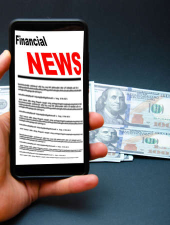 The smartphone on the screen the inscription financial news lies on dollars. 100 dollars banknotes and smartphone with financial news.の写真素材