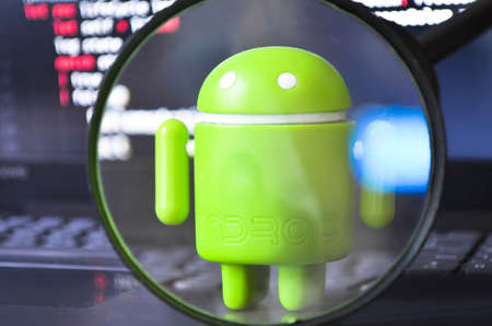 A green android figure on a white background and next to a yellow smartphone a view of it through a magnifying glass. Android and magnifying glass. July 2020. Kiev, Ukraineのeditorial素材