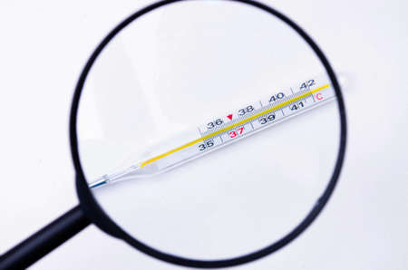 Mercury thermometer on a white background view through a magnifying glass. 36.6 temperature on a...