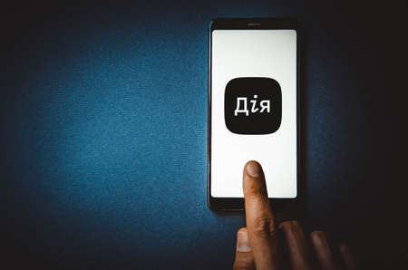 Diya. Smartphone in a man's hand on the Diya smartphone screen on a blue, yellow, black background. Ukraine in a smartphone.の写真素材