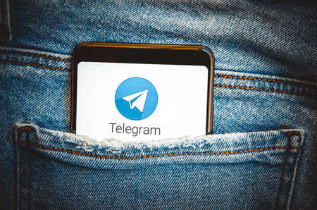 Telegram. Smartphone in the pocket of blue jeans on the Telegram smartphone screen on a blue,...