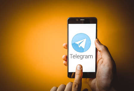 Telegram. Smartphone in a man's hand on the screen of a Telegram smartphone on a blue, yellow, black...