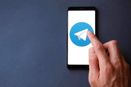Telegram. Smartphone in a man's hand on the screen of a Telegram smartphone on a blue, yellow, black background. July 2020. Kiev, Ukraine.のeditorial素材