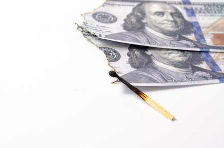 Burnt dollars. Burnt side view on a white background banknotes in close-up. A burnt match in the foreground.の写真素材