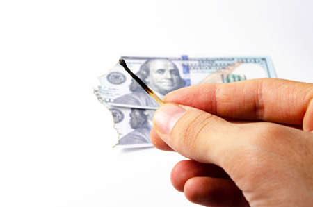 Burnt dollars. Burnt side view on a white background banknotes in close-up. A burnt match in the foreground. A match in a man's handの写真素材