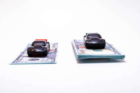 Two sports cars in black on two piles, piles of dollar bills podium. One pile, a pile more, another less. The difference in the price of the car. Buy, sell, rise and fall of prices in the marketの写真素材