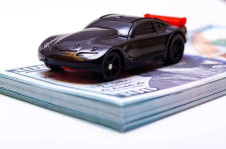 A toy sports car in black with a red wing on a springboard, a podium made of dollar bills. Car and dollars. Buying, selling price increases in the marketの写真素材