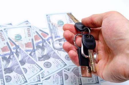 Two black keys with a leather keychain in close-up lie in a man's hand on the background dollars. Buying, selling real estate, apartment, house, car, businessの写真素材