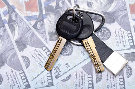 Two black keys with a leather keychain in close-up lie on dollars. Buying, selling real estate, apartment, house, car, businessの写真素材