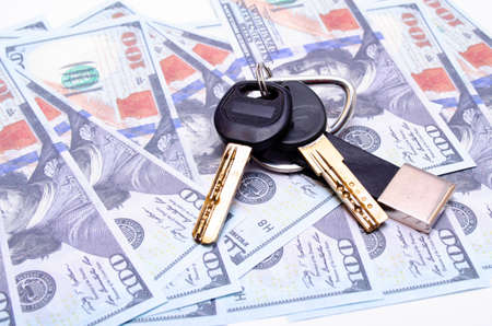 Two black keys with a leather keychain in close-up lie on dollars. Buying, selling real estate,...