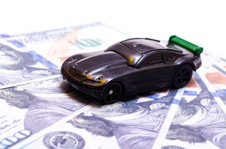 Black toy car on a heap of dollar bills on a white and black background. A sports car with a green spoiler, a wing on dollars in a close-up top and side view. Rear and front car. Selling, buyingの写真素材