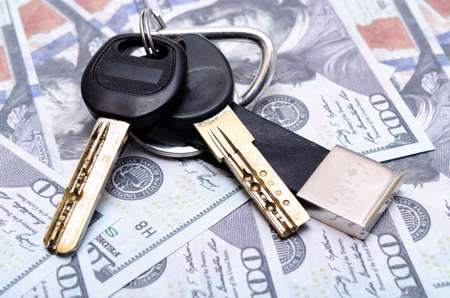 Two black keys with a leather keychain in close-up lie on dollars. Buying, selling real estate, apartment, house, car, businessの写真素材