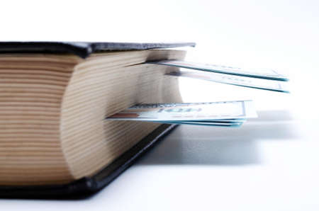 100 dollar bills lie in a black book on a white background in close-up. A man's hand opens a book...