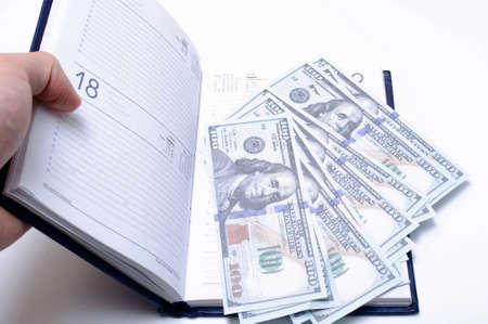 100 dollar bills lie in a blue notebook on a white background in close-up. A man's hand opens a notebook with dollars. Find, a stock for a rainy day dollars. Inheritanceの写真素材
