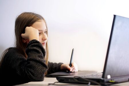 girl at home learns to draw on the laptop using a tablet and pen