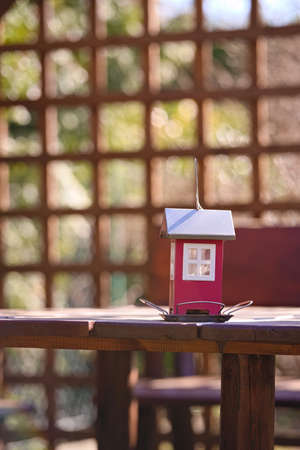 Red feeder for birds in the shape of a house on a background of openwork pergola in the gardenの写真素材