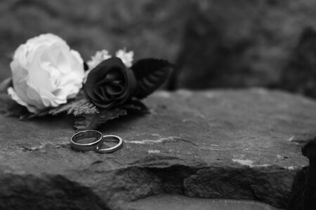 Two Wedding Rings with One Having a Message of Love Engraved Inside with a Blurred Flower and Rock Backgroundの写真素材
