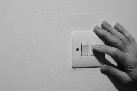 A Double Wall Light Switch, Showing a Natural Elderly Hand Switching off the Power Supply to Save Electricity in the UK.の写真素材