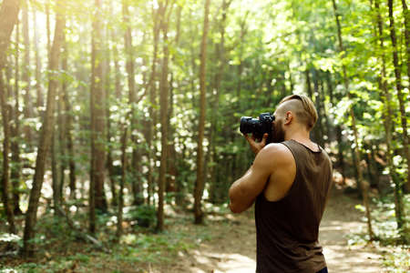 Bearded photographer man trekking among forest and taking pictures with dslr camera. Horizontal shape, copy spaceの写真素材