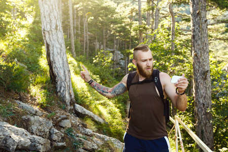 Bearded stylish hiker man using gps navigation for positioning at the mountain trail and thinks where to go. Technology conceptの写真素材