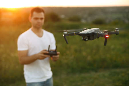 Drone hovers in front of man with remote controller in his hands. Quadcopter flies near pilot. Guy...