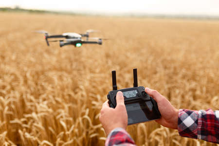 Man holds remote controller with his hands while copter is flying on background. Drone hovers behind...