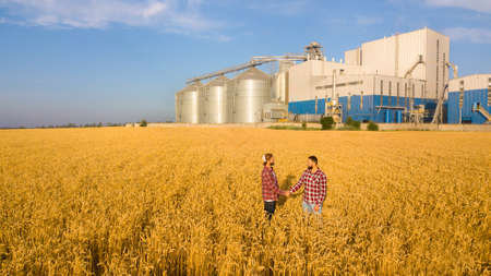 People shaking hands in a wheat field, farmers agreement. Grain elevator terminal on background. Agriculture agronomist business contract concept. Aerial photo. Agriculture themeの写真素材