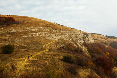 Group of three hikers going up the trail path. Wide shot of three backpackers climbing a mountans far from camera. Beautiful autumn sceneryの写真素材