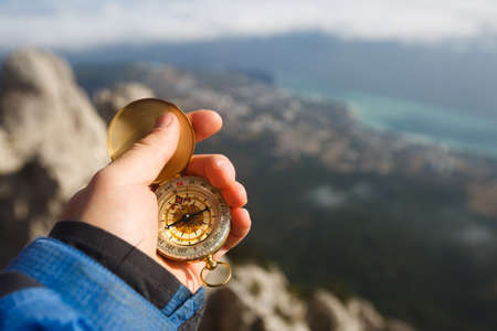Point of view photo of explorer man searching direction with golden compass in his hand above clouds...
