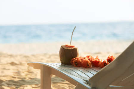 Coconut with drinking strawand lei flowers on beach bench or deck chair with blue ocean and white sand on background. Maldivesの写真素材