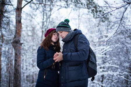 Young lovely couple warming up each others hands in snowy winter forest park.の写真素材